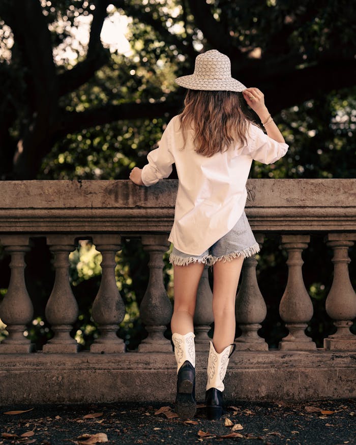 Home Stylish woman in denim shorts and cowboy boots standing at a balcony outdoors.