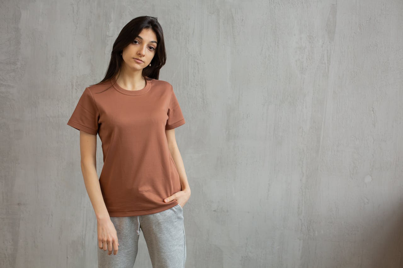 Home Serious female with long hair wearing t shirt and sweatpants standing against gray wall and looking at camera