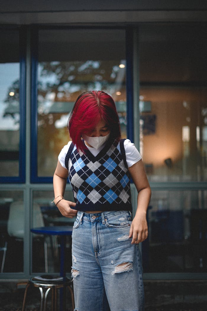 Home Stylish young woman with vibrant red hair wearing an argyle vest and ripped jeans.
